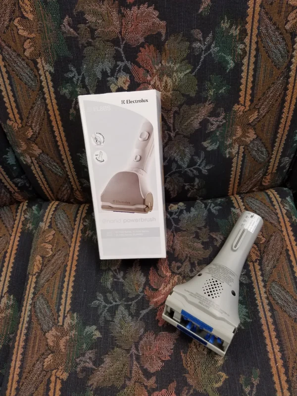 A white box sitting on top of a couch next to an electric shaver.