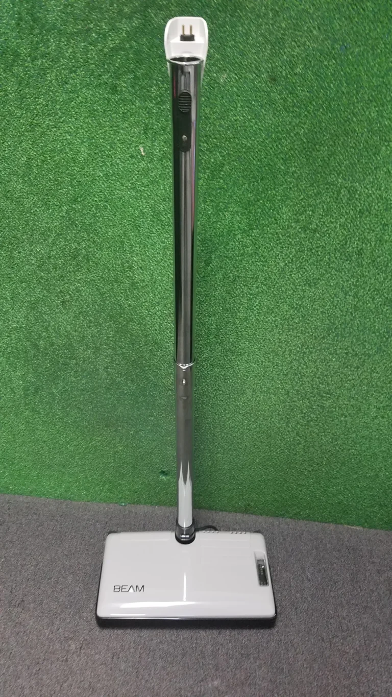A white and black vacuum cleaner on green grass.