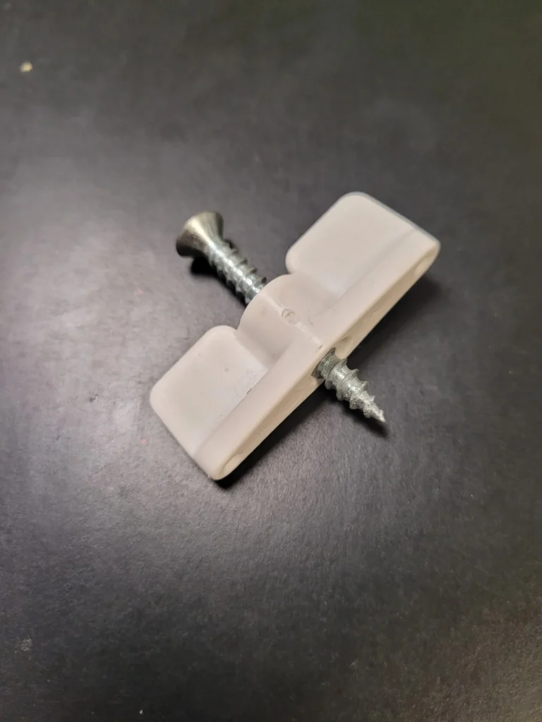 A white piece of plastic with a screw and one nail.