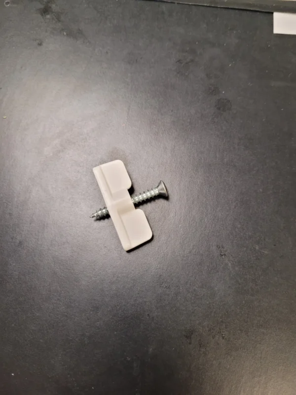 A white piece of plastic with a nail on it.