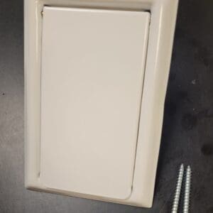 Wall plate with screws on a dark surface.